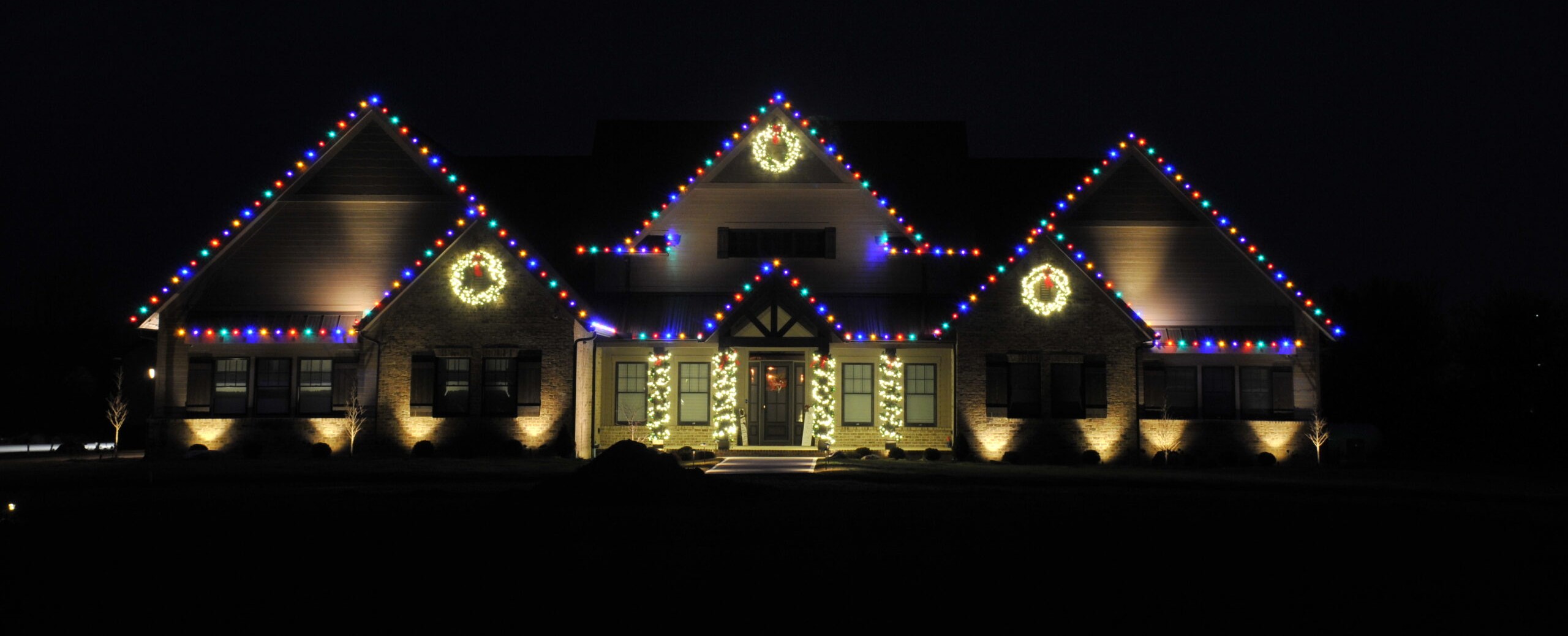 Home decorated with professional holiday lighting and illuminated wreaths at night